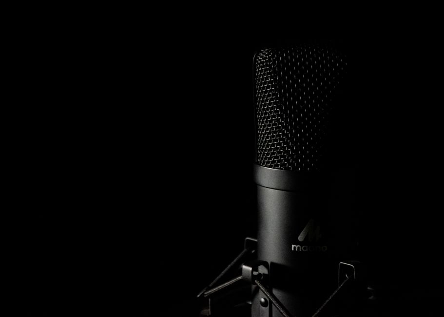 A black studio microphone lit from the side against a fully dark background, its metal grille catching the light