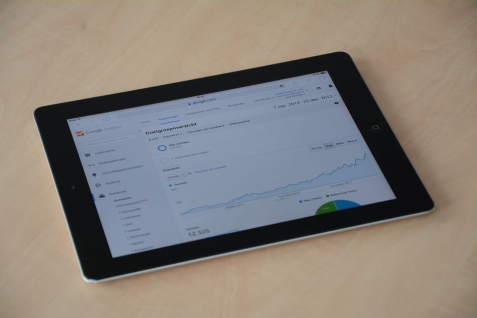 A tablet lying on a light wooden desk, its screen showing an analytics dashboard with a rising line chart and a pie chart
